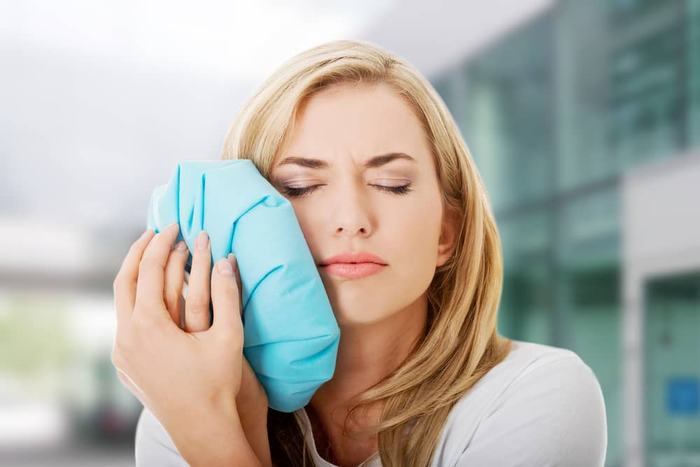 A woman holds an ice pack to her face for pain relief