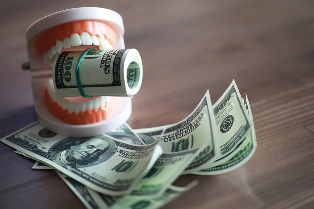 A denture bites down on a roll of dollar bills