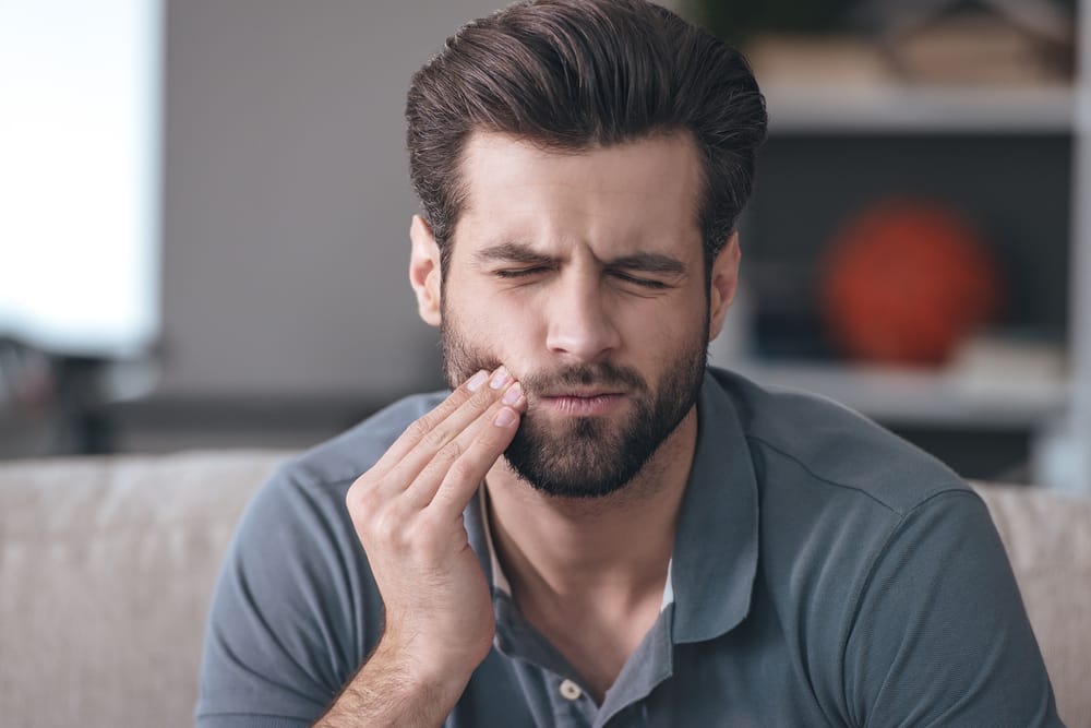 A man holds his cheek with tooth pain