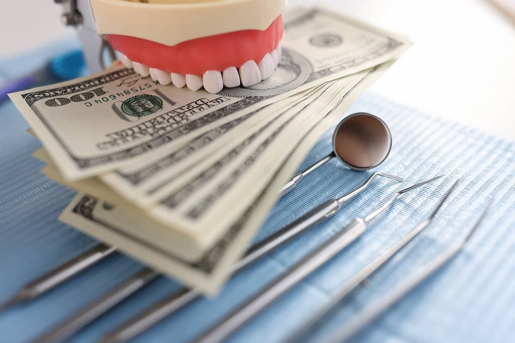 A denture bites down on a stack of 100 dollar bills.
