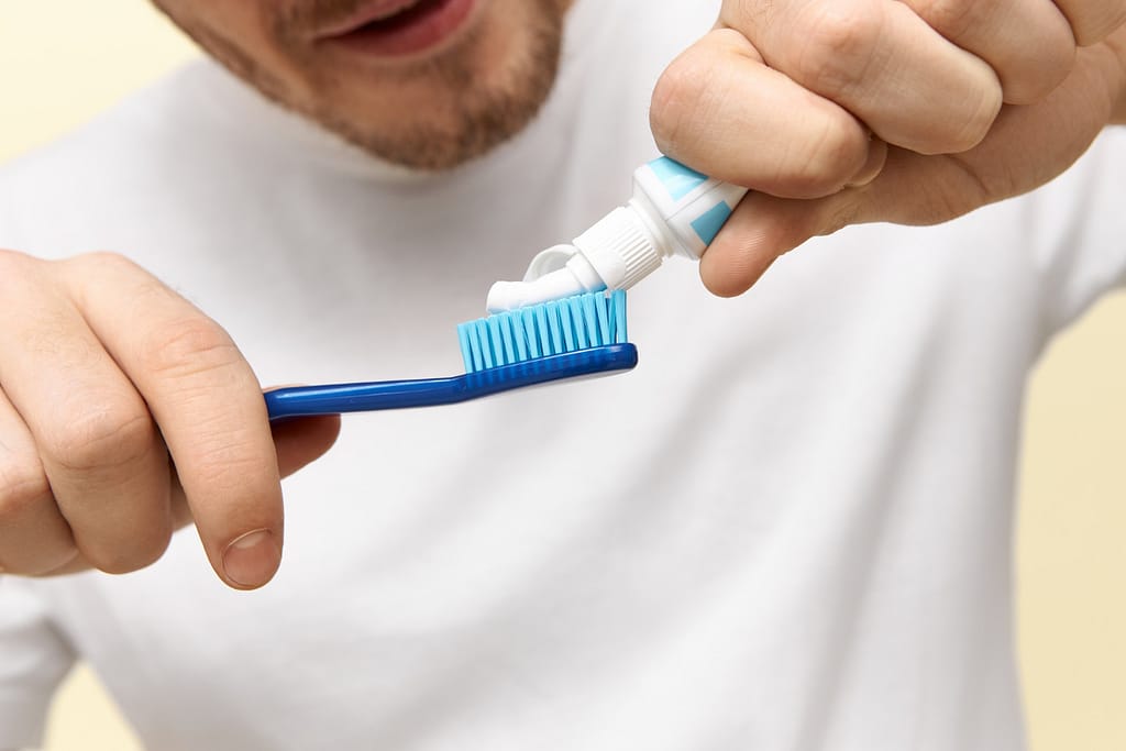 A man expresses fluoride toothpaste onto a toothbrush